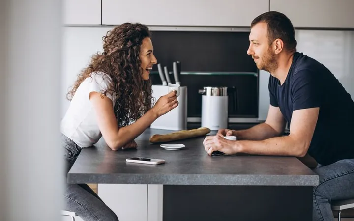 A man and a woman talking over coffee at the kitchen table