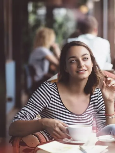 Woman at a café table with a cup of coffee, looking out at the street