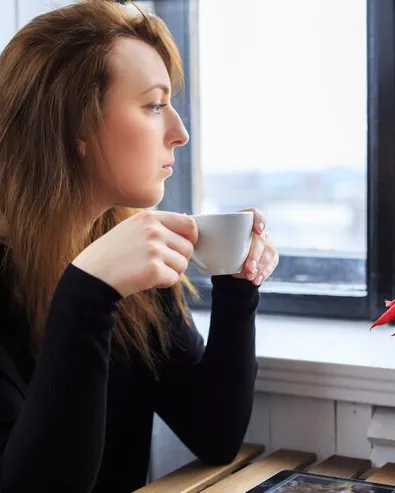 Woman drinking coffee by the window, looking outside