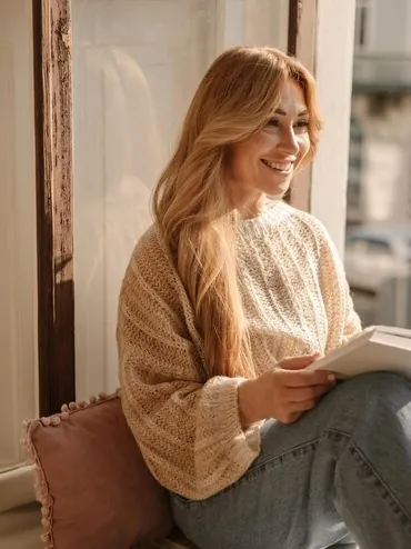 Woman reading a book by the window, smiling