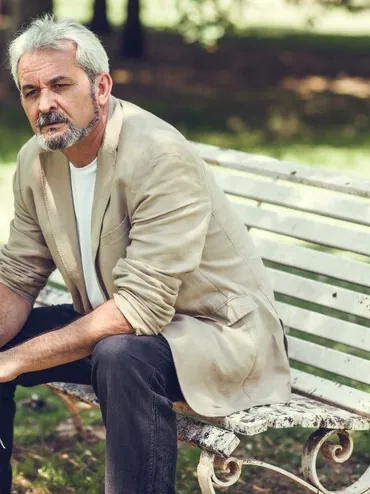 Grey-haired man sitting on a bench in the park