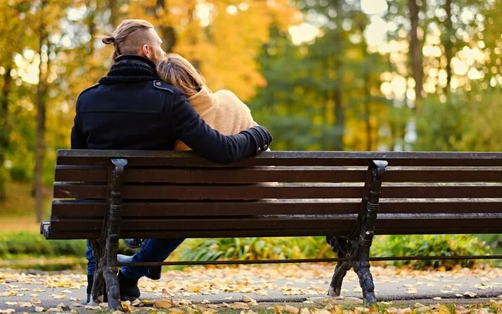 A couple seen from behind, on a park bench in autumn