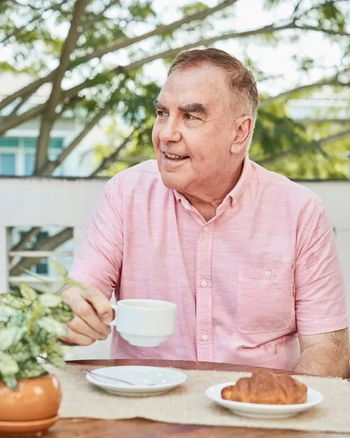 An older man with coffee and a croissant at a terrace table